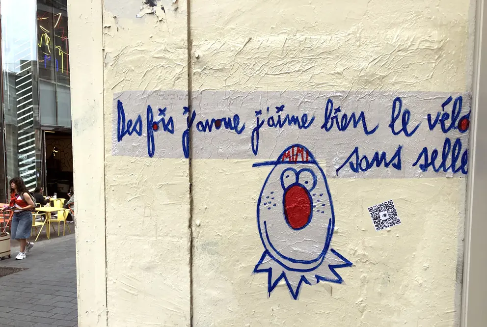 Collage urbain de MIMI the ClowN représentant un personnage au nez rouge accompagné de la phrase "des fois j'avoue j’aime bien le vélo sans selle", rue piétonne de Lille, juillet 2025.